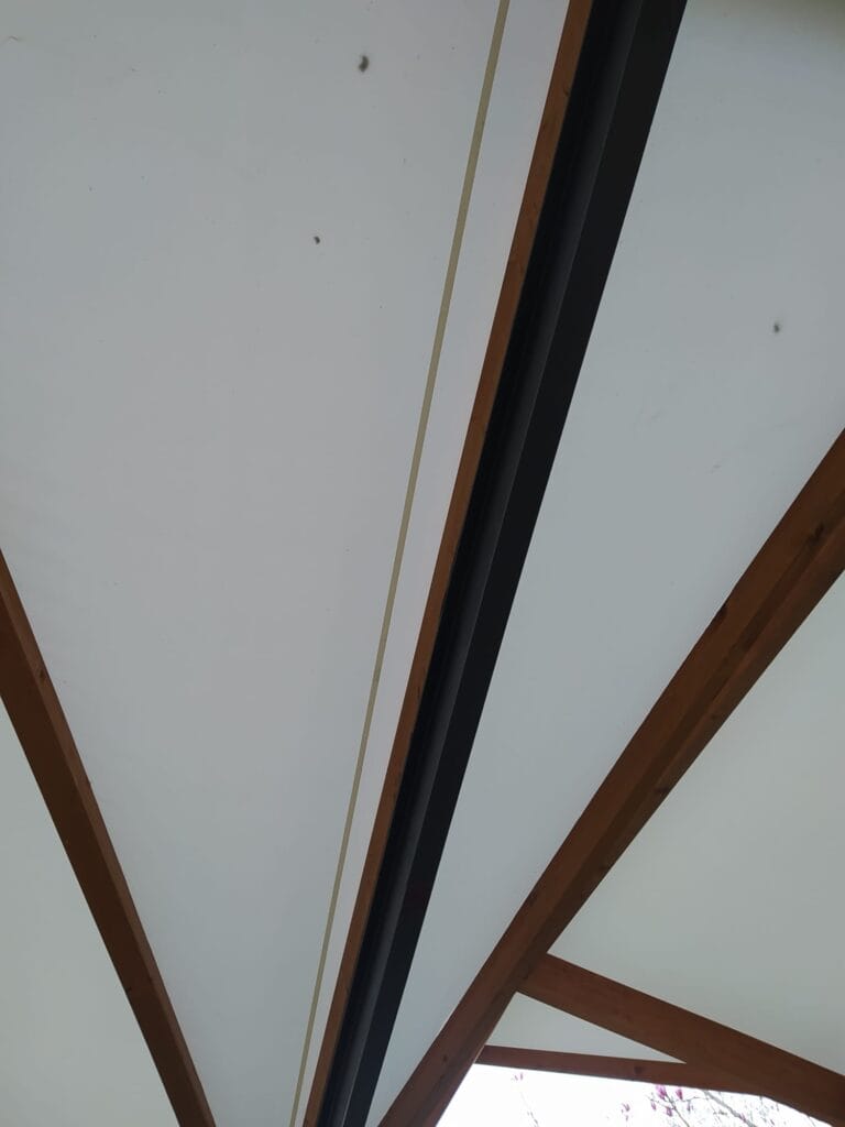 Patio cubierto con estructura de madera a base de geometría triangular y lona blanca.