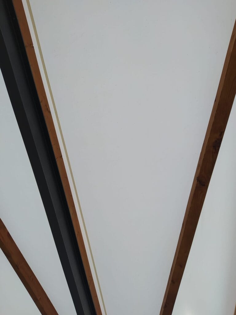 Patio cubierto con estructura de madera a base de geometría triangular y lona blanca.