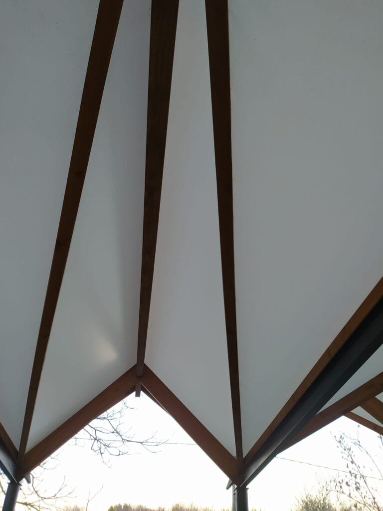 Patio cubierto con estructura de madera a base de geometría triangular y lona blanca.