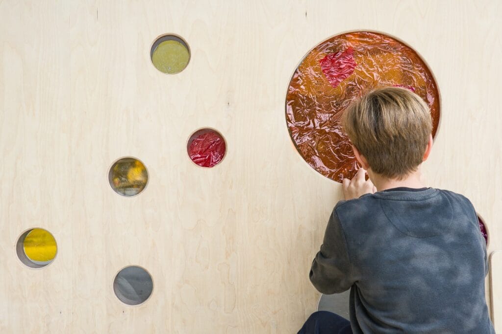 Niño jugando en una pared de madera con distintas opciones de juego.